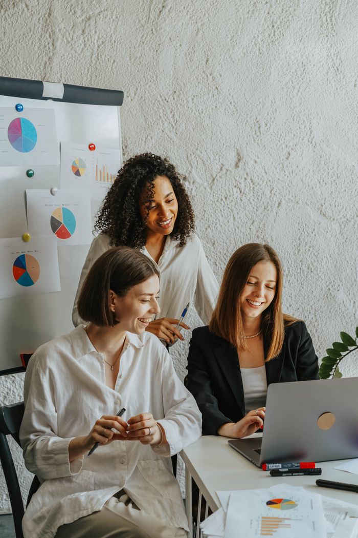Three businesswomen are working together around graphs and a laptop in a contemporary office environment.